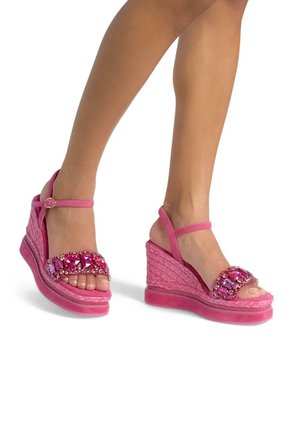 Pink wedge sandals with a textured material, embellished with large pink gemstones on the straps. Features ankle support and open toe design.
