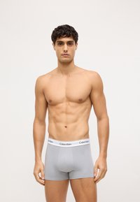 Szare bawełniane bokserki z białym paskiem z logo "Calvin Klein". Tkanina jest gładka i dobrze dopasowana.