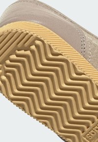 Κοντινή λήψη της μπεζ σόλας παπουτσιού με μοτίβο πέλματος σε ζιγκ ζαγκ και ραμμένο άνω άκρο σε ανοιχτό τάουπε χρώμα.