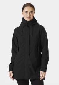 Chaqueta negra impermeable con cuello alto, cordones ajustables, dos bolsillos laterales y mangas largas. Textura suave y diseño sencillo.