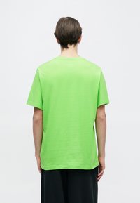 Πράσινο T-shirt με κοντά μανίκια και χαλαρή γραμμή· λεία υφή, στρογγυλή λαιμόκοψη, χωρίς αξιοσημείωτα σχέδια ή διακοσμητικά στοιχεία.