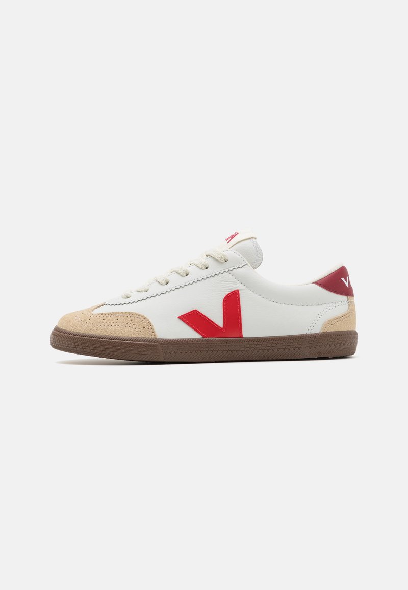 Sneaker bianco in pelle con logo e dettagli rossi, punta in suede beige, lacci crema e suola in gomma marrone con un motivo testurizzato.