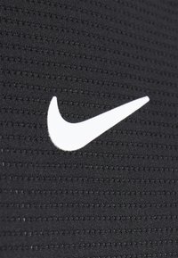 Tela negra con una superficie texturizada que presenta un logotipo de Nike en blanco, centrado de manera prominente. El material parece ligero y transpirable.