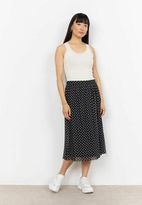 Valge pitsäärisega tank top, mis on kombineeritud musta midi seeliku ja valgete täppidega. Mudel kannab valgeid tenniseid, seistes ühevärvilise tausta ees.