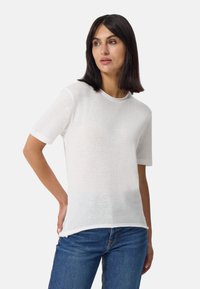 Witte katoenen t-shirt met korte mouwen, ronde hals, licht doorschijnende textuur en een ontspannen pasvorm, gecombineerd met blauwe denim jeans.