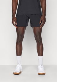 Korte zwarte sportshorts hebben een elastische tailleband en zijzakken. Gepaard met witte crew-sokken en witte sneakers met rubberen zolen.