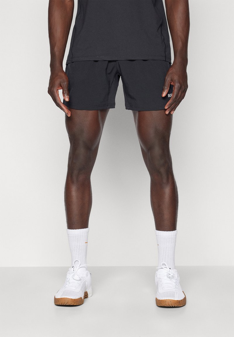 Korte zwarte sportshorts hebben een elastische tailleband en zijzakken. Gepaard met witte crew-sokken en witte sneakers met rubberen zolen.