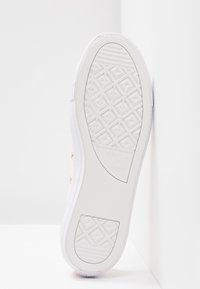 Semelle blanche de sneaker visible par en dessous, montrant un motif de bande de roulement texturé avec des formes géométriques et des bords blancs lisses.