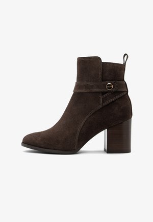 Brown suede ankle boot with a pointed toe, a decorative strap, and a block heel. Features contrast stitching and a pull tab at the back.