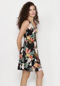 Blumenkleid mit schwarzem Hintergrund, versehen mit bunten Blumen und Blättern. Spaghetti-Träger, taillierter Oberteil und ausgestellter Saum.