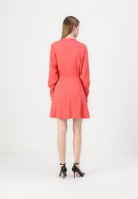 Coral long-sleeve dress with a fitted waist and flared skirt, made of smooth fabric. Paired with black ankle strap heels.