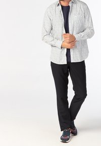 Biała koszula zapinana na guziki z małym niebieskim wzorem kwiatowym, zestawiona z czarnymi spodniami i ciemnymi trampkami. Koszula ma luźny krój i długie rękawy.