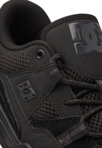 Zwarte sportschoen gemaakt van mesh en suede materialen. Voorzien van ronde veters, een metalen logo en een gevoerde kraag voor ondersteuning. Strak ontwerp.