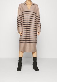 Šaty s dlouhým rukávem a výstřihem do V, vyrobené z měkké, béžové pleteniny s vodorovnými tmavě hnědými pruhy; délka ke kolenům s volnějším, rovně střihem.