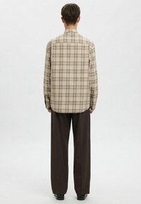 Beežila ruudulise mustriga pikkade varrukatega särk ümarate servade, nööpidega varrukaotsade ja ühe tagumise kaare detailiga, kombineeritud tumedate, laia säärega pükstega.