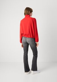 Rode trui met hoge kraag en elastische zoom, gecombineerd met donkergrijze flare jeans en witte sneakers. Effen stof en een relaxte pasvorm.