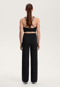 Černá sportovní souprava obsahující cropped top s podmínkovým zádovým designem a vysokým pasem, široké kalhoty. Hladká tkanina s minimálními detaily.