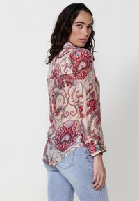 Blusa a maniche lunghe in tessuto trasparente, con fantasie floreali rosse e blu, colletto classico e polsini con bottoni.