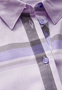 Gros plan sur un col de chemise lavande avec un motif à carreaux noirs et violet clair et trois boutons violets assortis fixés sur la patte de boutonnage.