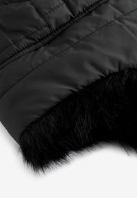 Tissu noir rembourré avec une douce bordure en fausse fourrure en bas ; texture lisse et couture détaillée à la surface.
