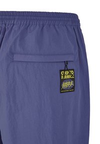 Lila Shorts aus leichtem Material, mit einem elastischen Bund und einer Gesäßtasche mit einem Logo-Patch in Gelb und Schwarz.