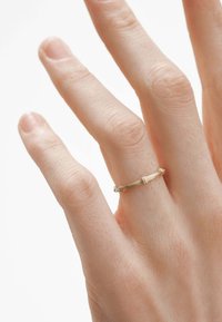 Anillo dorado en un dedo, con un delicado diseño texturizado que presenta un patrón retorcido y bordes suaves, sobre un fondo claro.