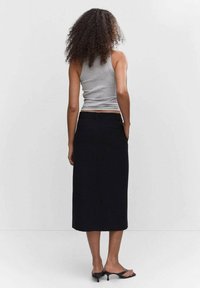 Jupe noire midi au design droit, confectionnée dans un tissu lisse. Comprend une fente à l'arrière et des poches. Portée avec un débardeur gris.