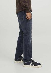 Vaqueros azul oscuro de corte recto, con un desvanecimiento sutil. Combinados con zapatillas negras y blancas, que muestran el sistema de cordones y una parte superior texturizada.