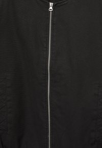 Crna bomber jakna izrađena od teksturirane tkanine. Sadrži srebrni prednji patentni zatvarač i akcentne dijamantske uzorke na bočnim džepovima.