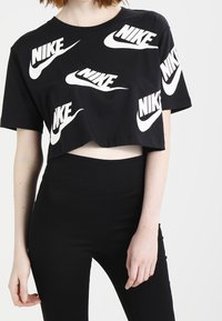 Svart kortärmad t-shirt i bomull med upprepade vita Nike-logotyper i olika orienteringar. Åtföljs av högmidjade svarta leggings.