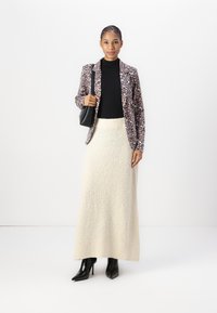 Leopard-print blazer, black turtleneck, cream maxi skirt with textured fabric, black handbag, and pointed black ankle boots.