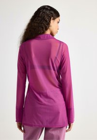 Transparent lilla langærmet top med krave, der har en glat tekstur og et forlænget bagstykke, suppleret med subtile sømdetaljer.