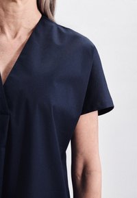 Mörkblå topp med kort ärm och V-ringning, med en mjuk yta, designad för en avslappnad passform. Har minimala sömmar och en enkel silhuett.