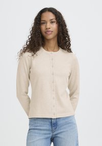 Bež jopica na gumbe z okroglim izrezom, dolgimi rokavi in gladko teksturo. Ima sprednjo zaporo z enakomerno razporejenimi gumbi.