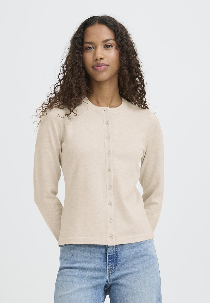 Bež jopica na gumbe z okroglim izrezom, dolgimi rokavi in gladko teksturo. Ima sprednjo zaporo z enakomerno razporejenimi gumbi.