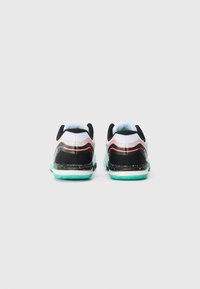 Zapatillas deportivas en blanco y negro con parte superior de malla, suela turquesa y acentos rojos, que presentan un diseño moderno y elegante con detalles texturizados.