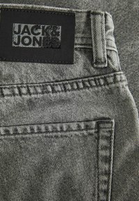 Närbild av grå denimjeansficka och bältesöggla med svart rektangulär Jack & Jones-märke som är sytt ovanför fickan.