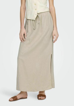 Falda maxi de lino beige con una abertura lateral y cintura elástica. Combinada con sandalias deslizantes de mimbre marrones. Tejido ligero y ajuste relajado.