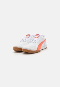 Des chaussures de sport blanches avec une surface texturée, présentant une bande Puma orange bien visible, une semelle en caoutchouc et des lacets de couleurs assorties.
