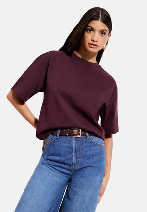 Bordeauxrotes kurzärmeliges T-Shirt mit rundem Ausschnitt, kombiniert mit hellblauen Jeans und einem braunen Gürtel. Baumwollstoff mit lockerer Passform.