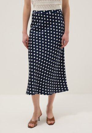 Falda midi azul marino con lunares blancos combinada con un top blanco de encaje y tacones marrones con punta abierta.