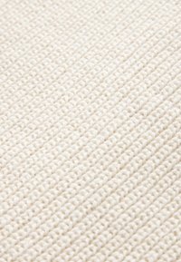 Teksturiran, off-white material z z woven vzorom. Površina ima mehak, rebrast dizajn, ki prikazuje nežni, lahki videz.