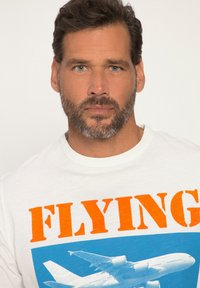 White cotton t-shirt featuring bold orange text reading "FLYING" and a blue graphic of an airplane below the text.