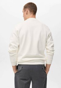 Sudadera color crema con cuello redondo, puños acanalados y corte holgado, combinada con pantalones gris oscuro que tienen bolsillos traseros.