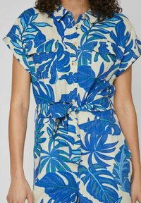 Košilové šaty s modro-zeleným listovým vzorem z lehkého materiálu, se zapínáním na knoflíky vpředu, krátkým rukávem a zavázaným pasem.