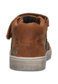 Bruine suède hoge schoen met klittenbandsluiting, textuur bovenkant, contrasterend zwart paneel, witte rubberen zool en groene stikselaccenten.