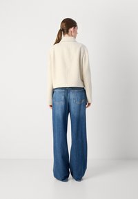 Lichtbeige cropped jack met een gestructureerde afwerking, gecombineerd met hoge taille, wijde spijkerbroeken van blauw denim. De outfit heeft een eenvoudig ontwerp.