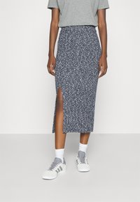 Neulottu midi-hame tummansinisenä, jossa on kuvioitu pinta ja sivuhalkio. Yhdistetty harmaaseen t-paitaan ja valkoisiin urheilukenkäisiin.