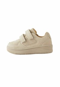 Baskets en velcro beige avec une texture en suède douce, présentant une pointe arrondie et une semelle robuste, sur un fond blanc uni.