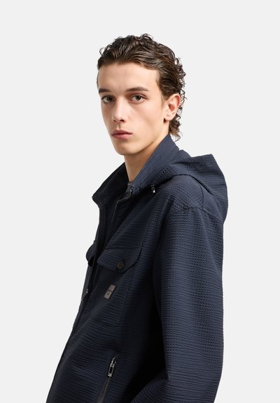 Giacca con cappuccio in blu navy strutturato, dotata di due tasche frontali, chiusura con zip e cordino regolabile, caratterizzata da un motivo sottile.